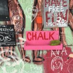 Colourful graphitti wall with messages involving discounts, Free Palestine, doodles. It has a prominent pink shelf in centre that reads CHALK. On it is a green sponge, but no chalk.