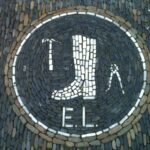 Stone mosaic showing a boot, hammer, pliers and the letters 'E. L.'