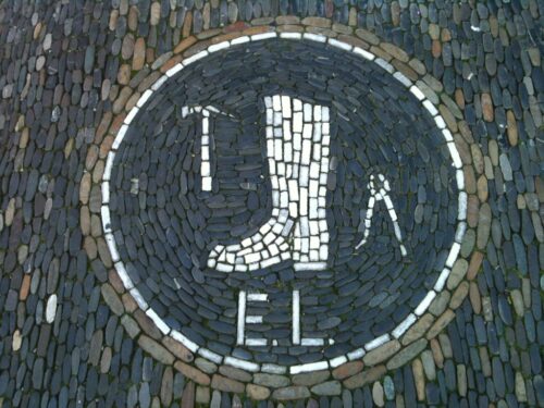 Stone mosaic showing a boot, hammer, pliers and the letters 'E. L.'