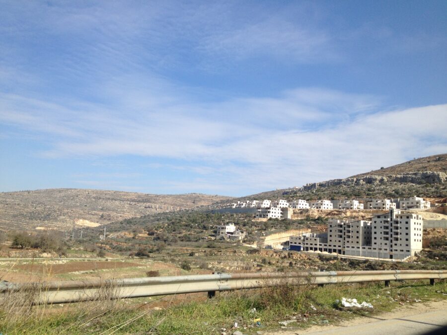 Photo of a white Israeli buildings, perhaps a settlement, set against a Palestinian landscap