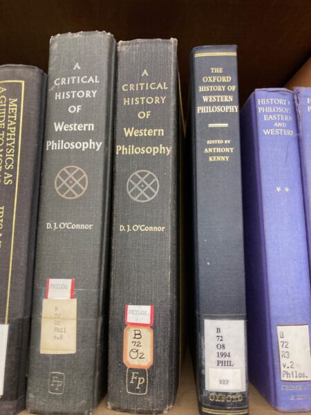 Spines of books on shelves with titles 'A Critical History of Western Philosophy', 'THe Oxford History of Western Philosophy', 'History of Philosophy Eastern and Western'