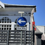 Blue one way street sign pointing left with white building behind