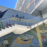 White outdoor stairs leading into an appartment block with image of rowers on wall behind