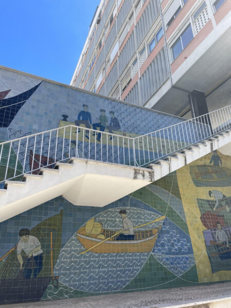 White outdoor stairs leading into an appartment block with image of rowers on wall behind